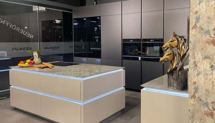 Ausstellungsfoto einer modernen schwarzen Küche mit weißer Kücheninsel. Integrierte indirekte Beleuchtung sorgt für eine angenehme Atmosphäre.