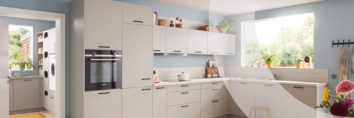 Helle, moderne Küche in Beige und Weiß mit hellem Holzboden. Im Vordergrund stehen ein runder Esstisch und ein gepolsterter Stuhl.
