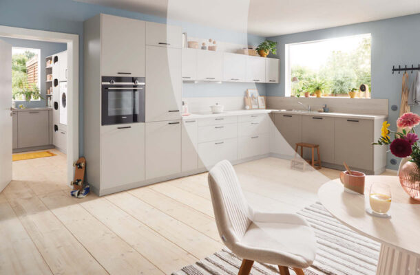 Helle, moderne Küche in Beige und Weiß mit hellem Holzboden. Im Vordergrund stehen ein runder Esstisch und ein gepolsterter Stuhl.