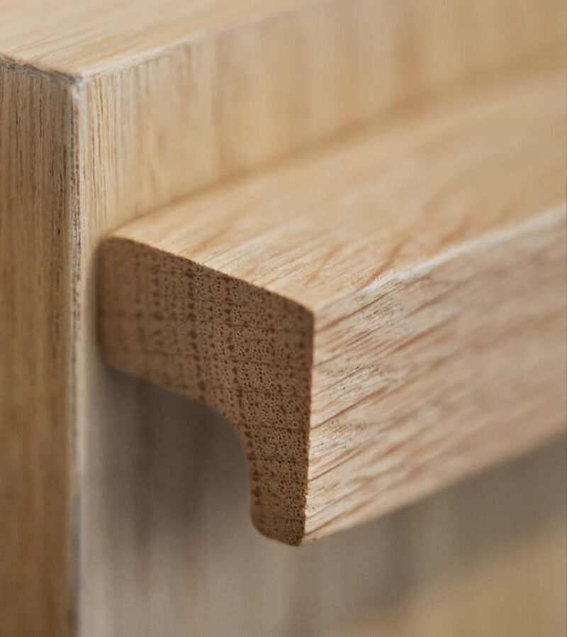 Makroaufnahme eines eingelassenen Holzgriffs (wahrscheinlich Eiche) an einer Möbelfront. Die Aufnahme zeigt die natürliche Maserung und das abgerundete Profil der Griffleiste.