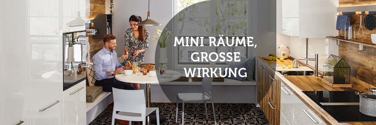 Helle, weiße Küche mit Holzakzenten und dunklem Musterboden. Ein Paar sitzt an einem kleinen Esstisch. Text-Overlay: "MINI RÄUME, GROSSE WIRKUNG".