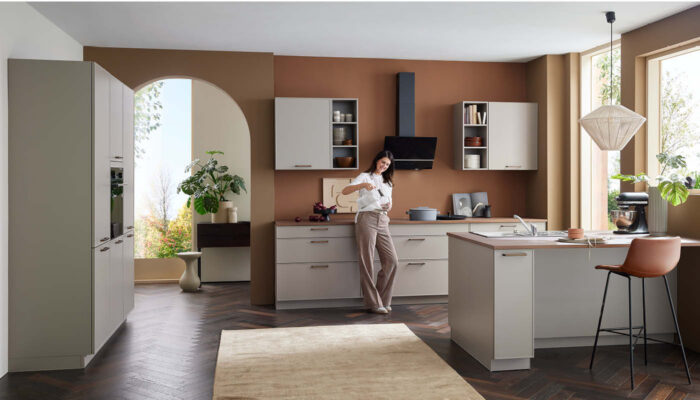 Frau steht in heller Küche mit brauner Akzentwand und modernen Fronten – elegante Küche in deutscher Fertigungsqualität.