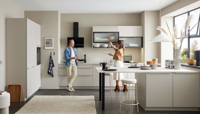 Helles Küchendesign mit großem Fenster und zwei Personen beim Kochen – moderne deutsche Küchenqualität.
