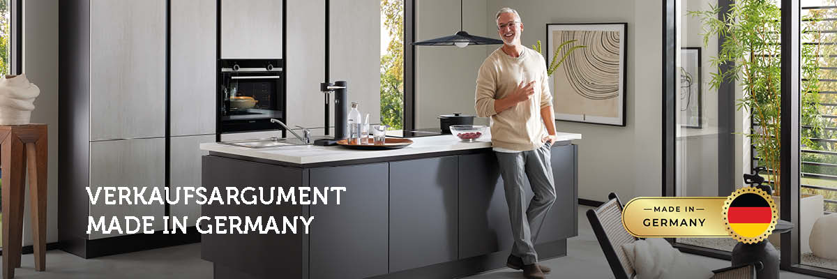 Moderner Mann in heller Küche mit Kücheninsel und großem Fenster – Symbolbild für Qualität und Design „Made in Germany“.