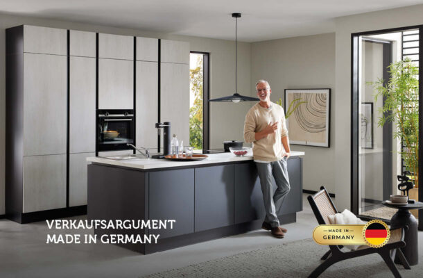 Moderner Mann in heller Küche mit Kücheninsel und großem Fenster – Symbolbild für Qualität und Design „Made in Germany“.