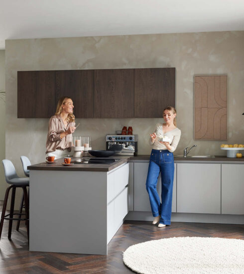 Zwei Frauen unterhalten sich in moderner Küche mit dunklen Holzfronten – stilvolles deutsches Küchendesign mit Wohlfühlatmosphäre.