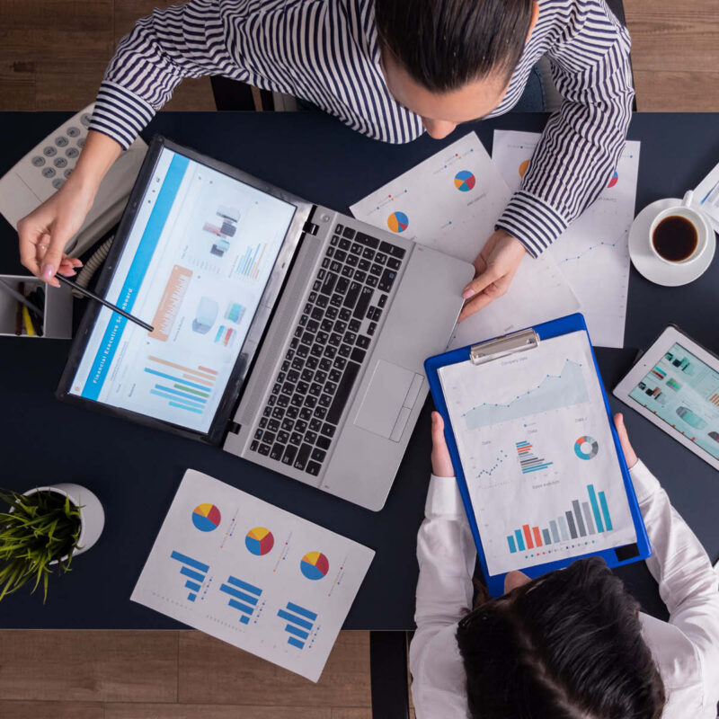 Zwei Personen arbeiten an Laptop und Diagrammen – Teamarbeit und Datenanalyse im modernen Unternehmensumfeld.