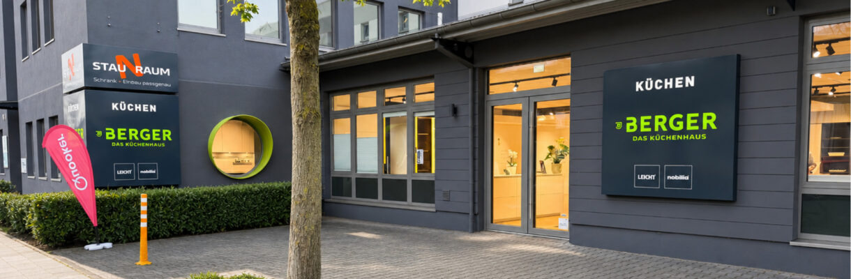 Modernes Küchenstudio Berger Das Küchenhaus in Duisburg mit gepflegter Außenansicht, großen Schaufenstern und beleuchtetem Eingangsbereich bei freundlichem Tageslicht.