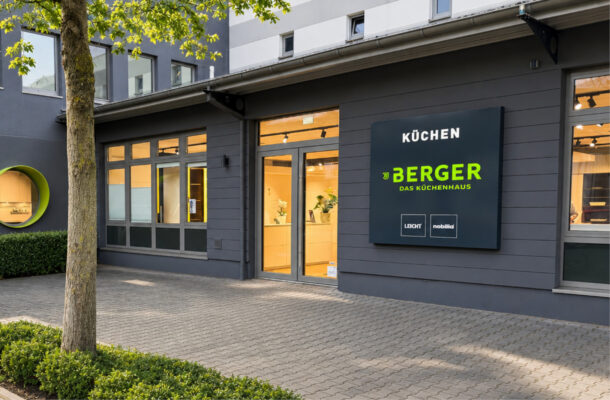 Modernes Küchenstudio Berger Das Küchenhaus in Duisburg mit gepflegter Außenansicht, großen Schaufenstern und beleuchtetem Eingangsbereich bei freundlichem Tageslicht.