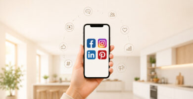 Hand hält ein Smartphone vor einer modernen, hellen Küchenumgebung. Auf dem Display sind die Logos von Facebook, Instagram, LinkedIn und Pinterest zu sehen. Um das Smartphone herum symbolisieren verschiedene Icons digitale Marketingaktivitäten wie Kommunikation, Reichweite, Interaktion, Analyse und Content-Erstellung in sozialen Netzwerken.