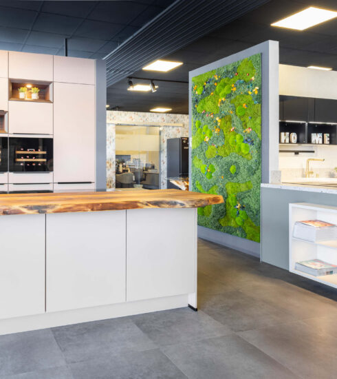 Großzügiges Küchenstudio mit moderner Küchenzeile, Massivholz-Theke, Einbaugeräten, beleuchteter Mooswand und Ausstellungsbereich für Designküchen