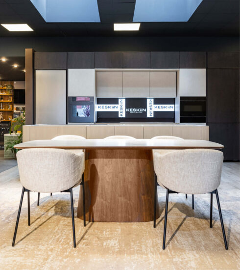 Wohnliche Designküche im Küchenstudio mit dunklen und hellen Küchenfronten, integrierten Einbaugeräten, Esstisch und gepolsterten Stühlen
