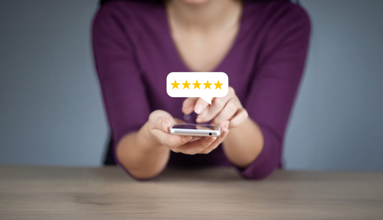 Frau hält ein Smartphone in der Hand und gibt eine Bewertung mit fünf gelben Sternen ab, die in einer Sprechblase über dem Gerät angezeigt werden.