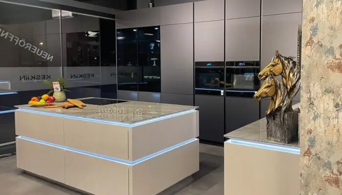 Ausstellungsfoto einer modernen schwarzen Küche mit weißer Kücheninsel. Integrierte indirekte Beleuchtung sorgt für eine angenehme Atmosphäre.