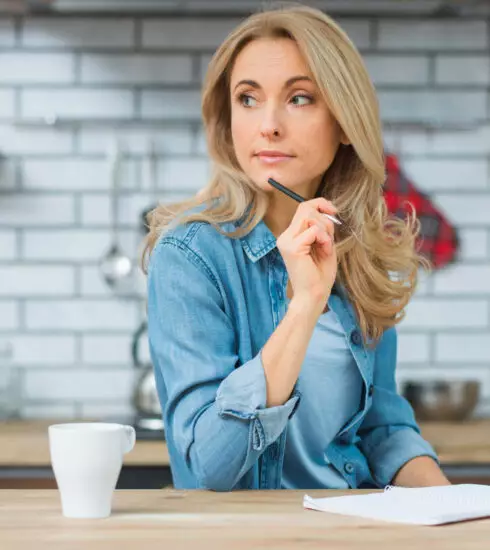 Blonde Frau in einer Küche denkt mit einem Stift am Kinn nach. – Premium Preisstrategie