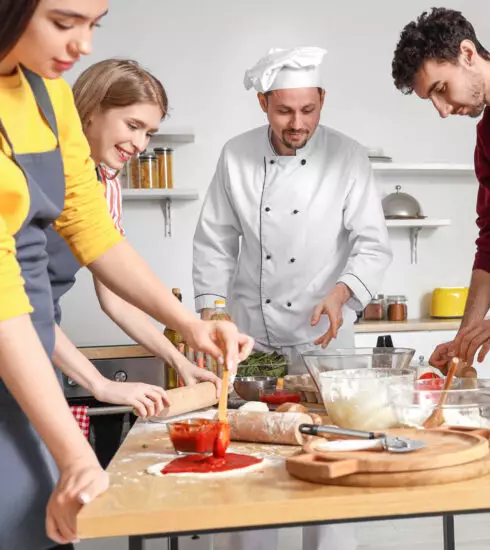 Gruppe von jungen Menschen lernt von einem Koch das Pizza backen.