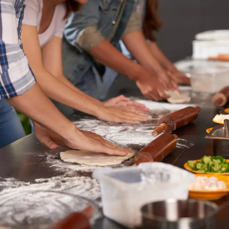 Viele Hände nebeneinander bereiten Pizzateig zum belegen in einem Event zum Kochen vor.