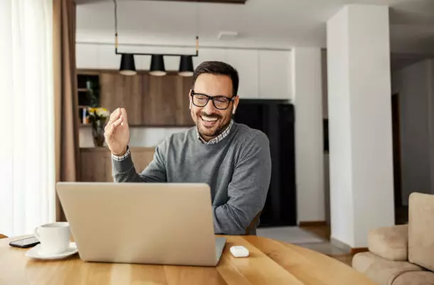 Ein Mann sitzt in seiner Küche am Esstisch und hat einen Videocall