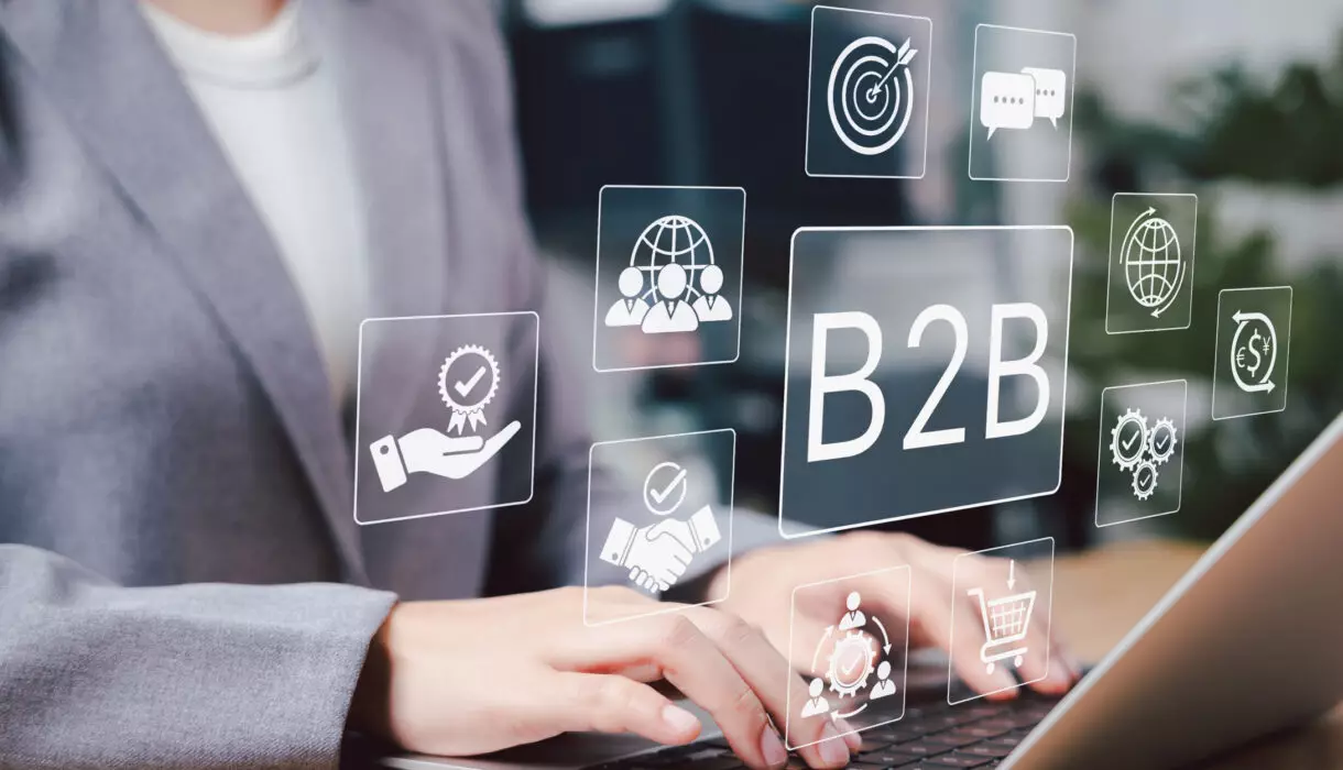 Person am Laptop mit eingeblendeten Symbolen für B2B-Vernetzung, Kommunikation und Zusammenarbeit.