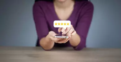 Frau hält ein Smartphone in der Hand und gibt eine Bewertung mit fünf gelben Sternen ab, die in einer Sprechblase über dem Gerät angezeigt werden.