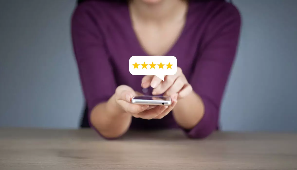 Frau hält ein Smartphone in der Hand und gibt eine Bewertung mit fünf gelben Sternen ab, die in einer Sprechblase über dem Gerät angezeigt werden.
