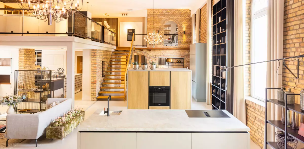 Modernes Küchenstudio von Mauermann Küchen mit großzügiger Kochinsel, hochwertigen Küchenmöbeln, offenen Galerien und stilvollen Backsteinwänden.