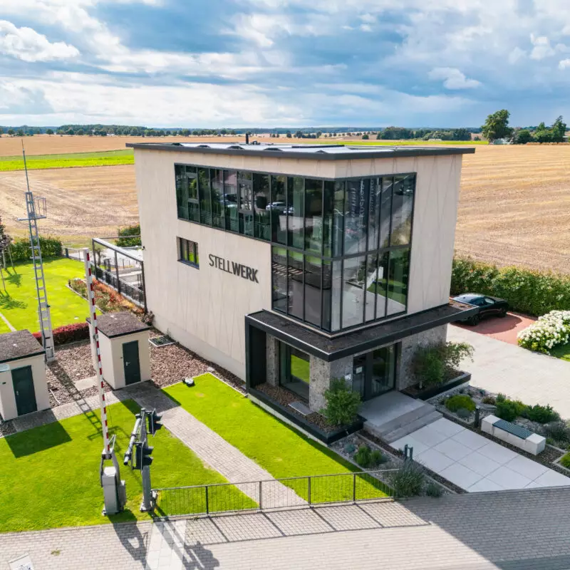 Luftaufnahme des modernen Firmengebäudes STELLWERK von Mauermann Küchen mit großer Glasfassade, gepflegter Außenanlage und umliegenden Feldern.